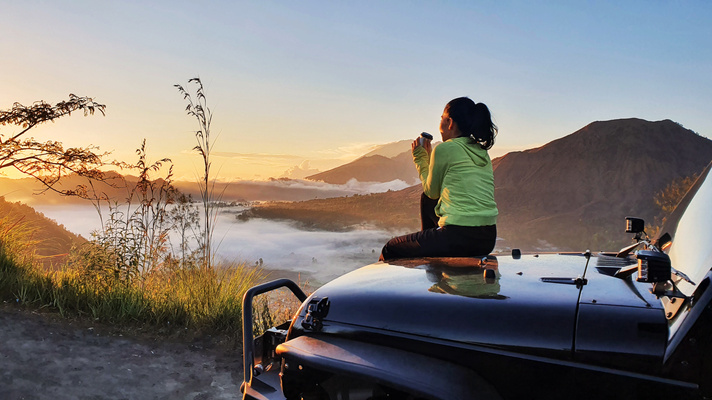 Woman Sitting on the Car Hood Looking at Mount Batur